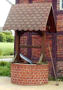 Dorfstrasse neben der Feuerwehr - ein Brunnen im alten Stil mit Dach und Zugvorrichtung für den Eimer